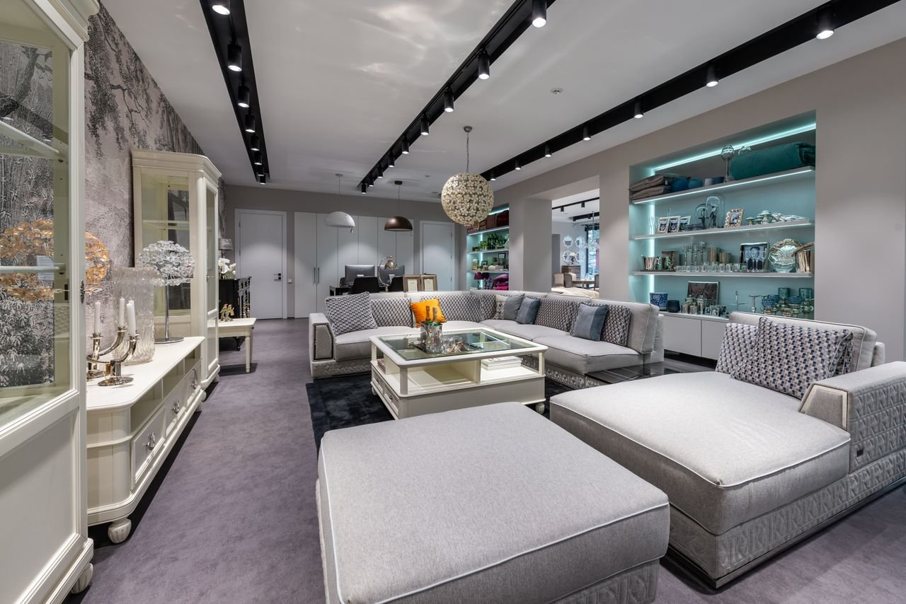 Comfortable sofa with cushions near table placed in spacious modern apartment with white cabinet and various decorative elements on shelves